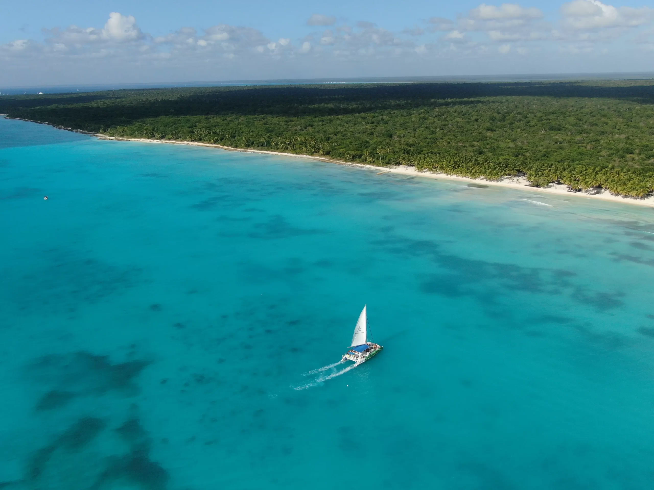 Catamaran rental in Cancun sailing across turquoise Caribbean waters near a tropical coastline, ideal for private cruising and island trips.
